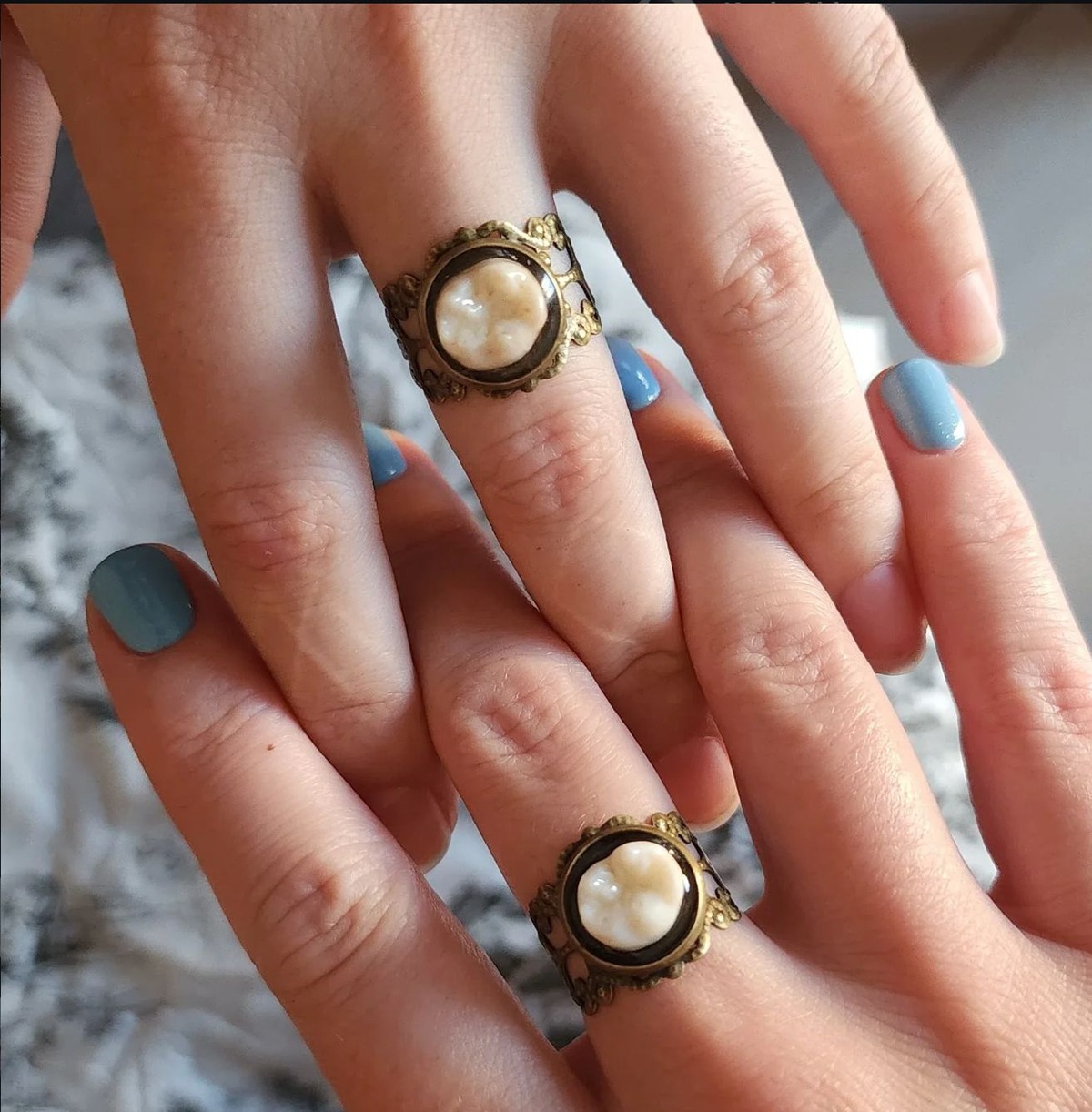 Two personal baby tooth keepsake rings held in a hand, showing past work by Pretty Dead Decor.