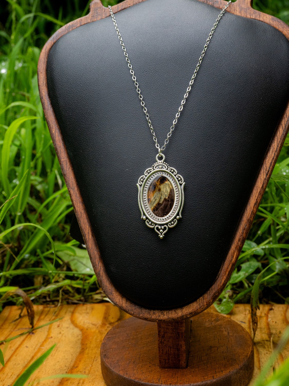 Butterfly wing necklace · III. A butterfly wing in an ornate oval pendant with a light metallic finish.